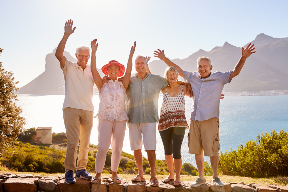 A group of people standing next to each other. They are waving their hands in the air. And there is water behind them. And mountains on either side of the lake.